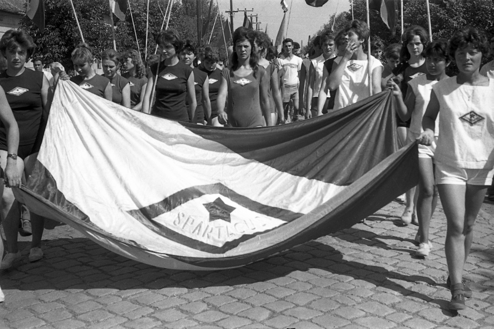 Hungary, Kisújszállás, Rákóczi utca az Illésy utca felől a Csatorna utca felé nézve., 1960, Morvay Kinga, Morvay Lajos, flag, march, cobblestones, athletic dress, Fortepan #84449