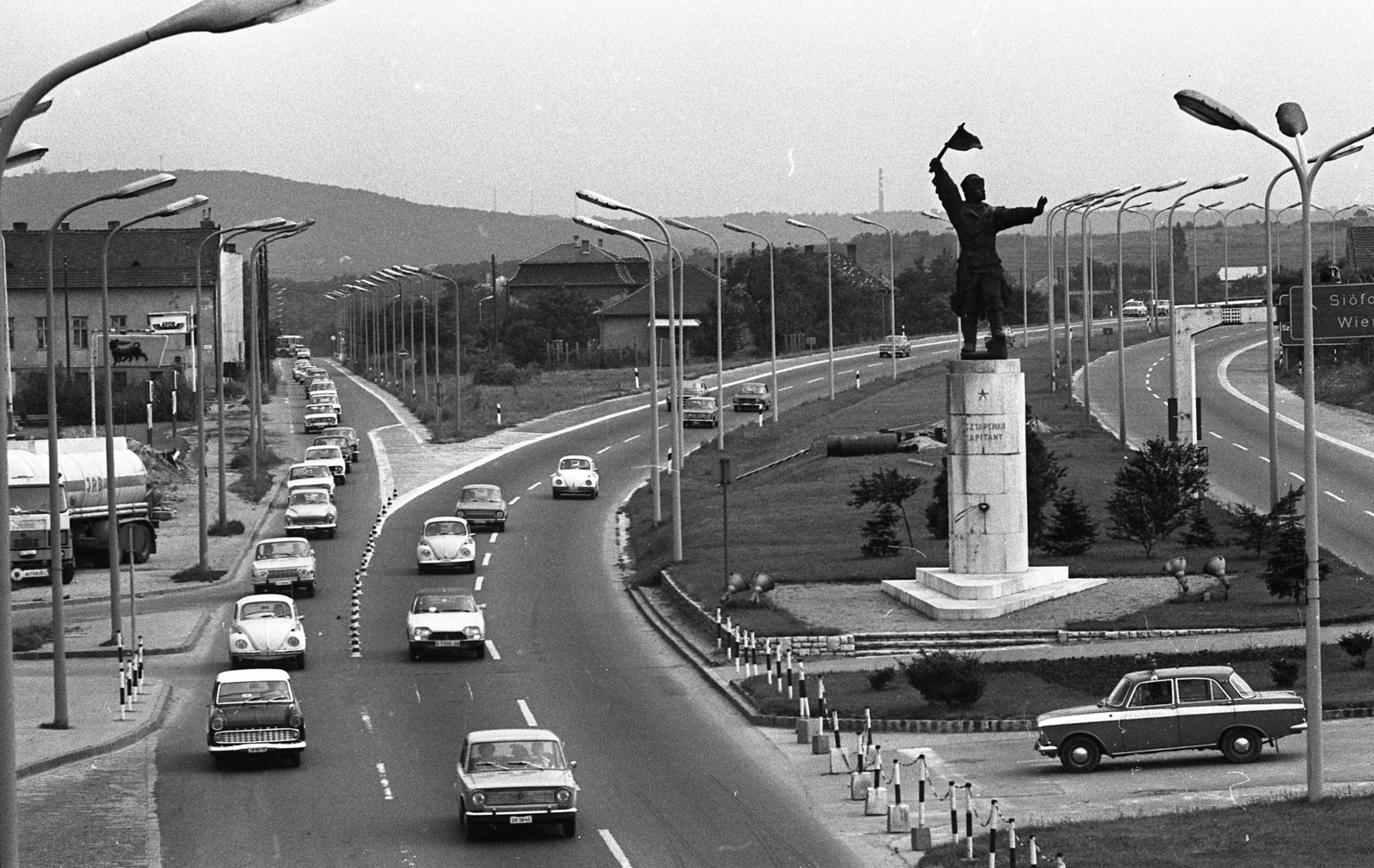 Magyarország, Budapest XI., Osztapenko szobor a Balatoni út és az M1-M7 közös szakaszánál a Budaörsi út irányából nézve., 1976, Urbán Tamás, szobor, útjelző tábla, Lada-márka, Volkswagen-márka, Ford-márka, Citroen-márka, rendőrjármű, Agip-márka, Osztapenkó-ábrázolás, Budapest, Fortepan #89303