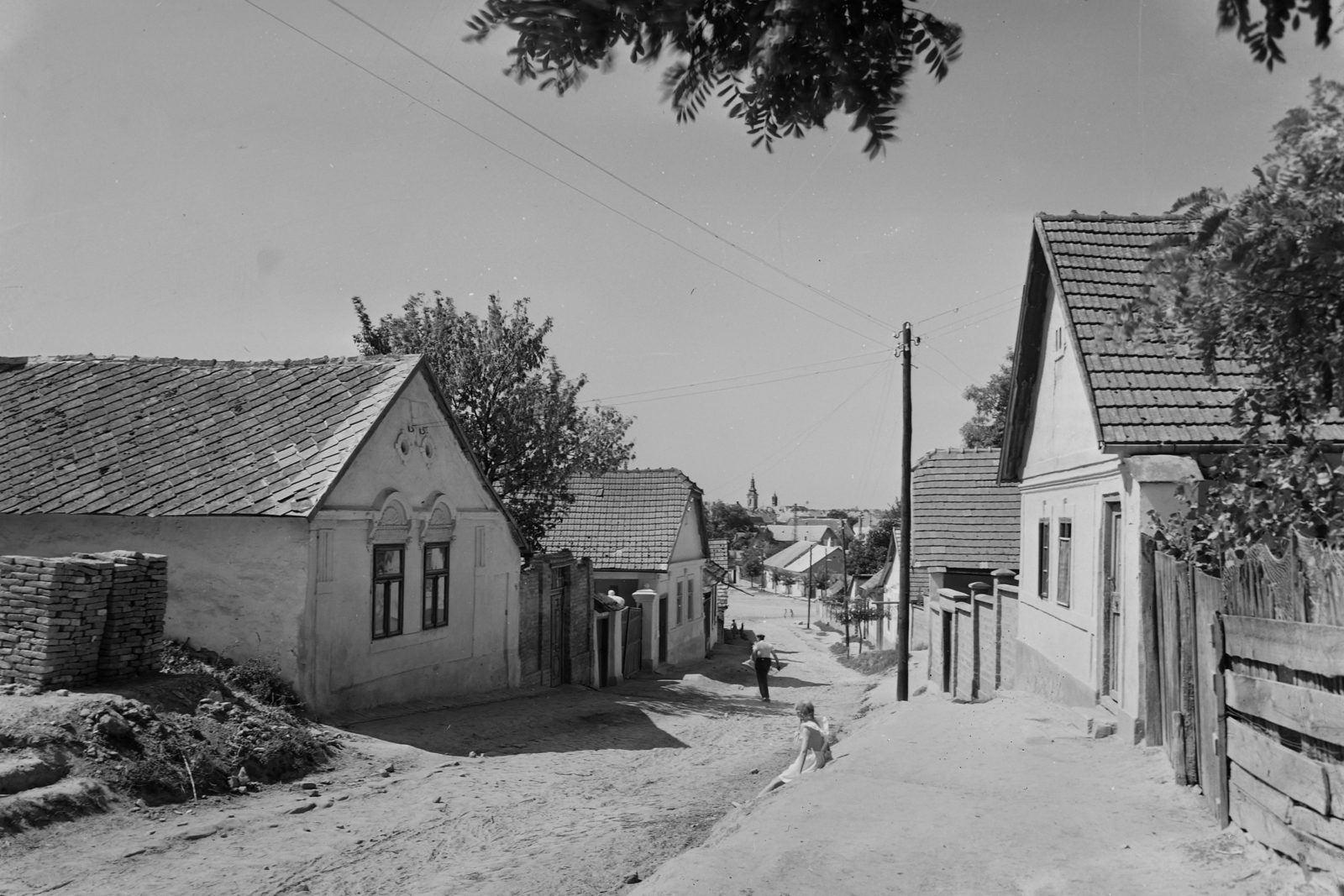 Hungary, Dunaföldvár, Alsó Burgundia utca, háttérben a szerb templom tornya és a Tanácsháza (később Városháza) huszártornya látszik., 1955, UVATERV, egy dunai hajóút, street view, architectural ornament, dirt road, village, Fortepan #91066