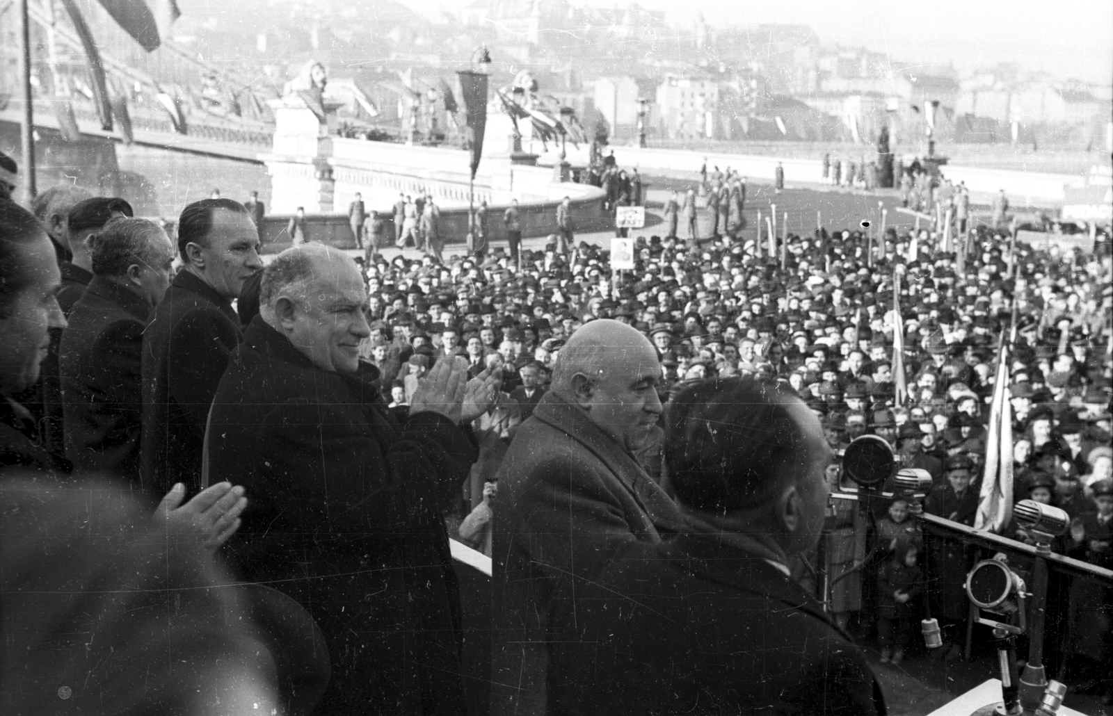 Hungary, Budapest V., Széchenyi István (Roosevelt) tér. Az újjáépített Széchenyi Lánchíd átadási ünnepségének tribünje, középen Rákosi Mátyás, tőle balra Bebrits Lajos és Kádár János., 1949, UVATERV, celebrity, flag, mass, festive, politics, microphone, grandstand, speech, clapping, stone lion, Budapest, Duna-bridge, politician, Fortepan #92015