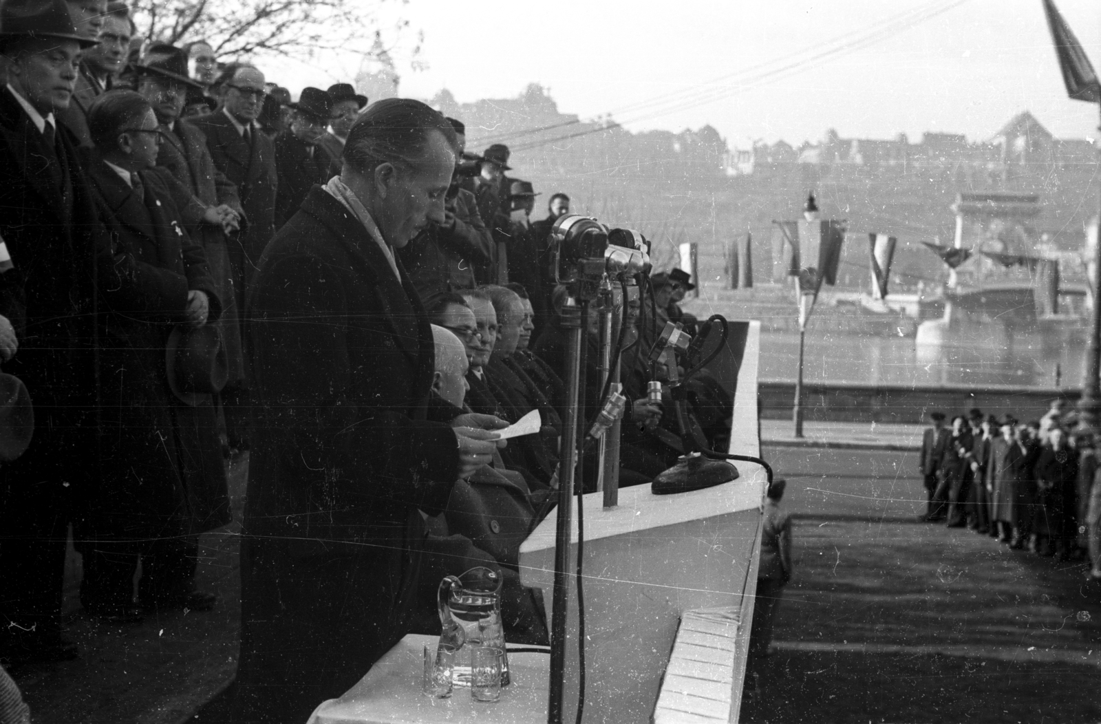 Hungary, Budapest V., Széchenyi István (Roosevelt) tér. Az újjáépített Széchenyi Lánchíd átadási ünnepségének tribünje. A mikrofonnál Palotás László építőmérnök / hidász, a híd újjáépítési munkálatainak vezetője., 1949, UVATERV, celebrity, mass, festive, politics, grandstand, speech, Budapest, Duna-bridge, bunting, politician, Fortepan #92016