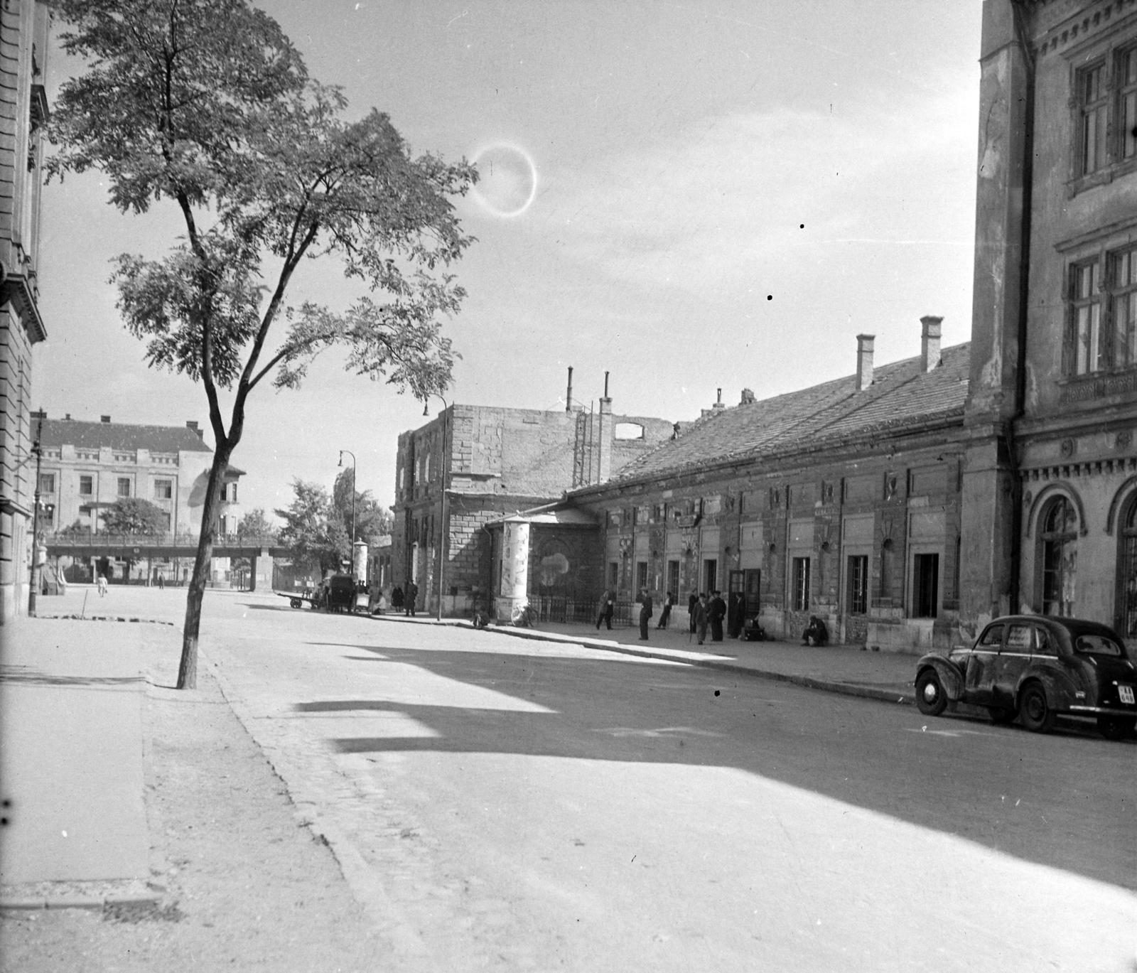 Hungary, Győr, Révai Miklós utca, jobbra a lebombázott vasútállomás, háttérben a Baross (Lenin) híd., 1950, UVATERV, street view, genre painting, ad pillar, lamp post, train station, handbarrow, automobile, number plate, Ferenc Pfaff-design, Fortepan #96617