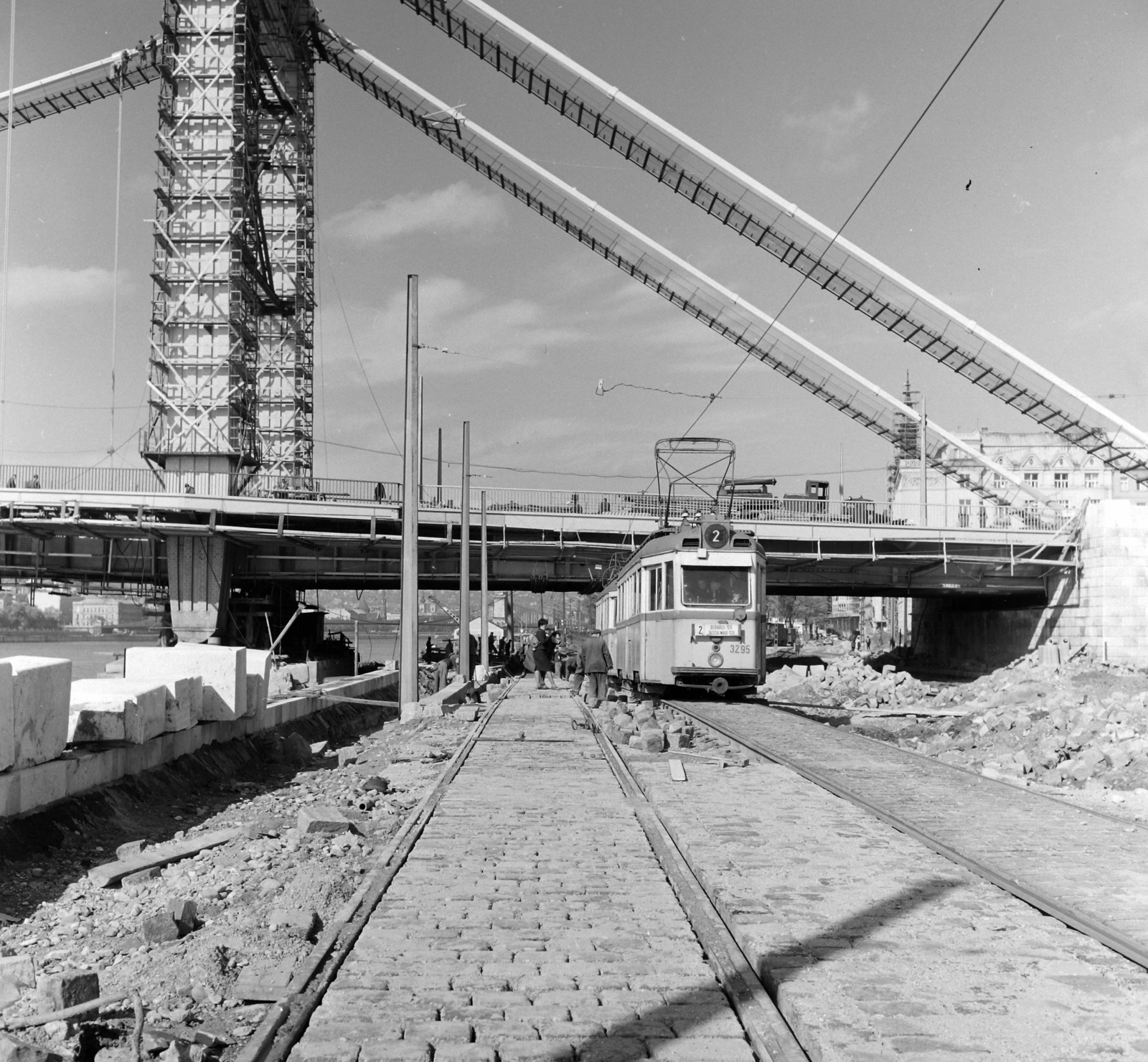Hungary, Budapest V., az épülő Erzsébet híd pesti hídfője a Március 15. tér előtti rakpartról nézve. Távolban az ortodox székesegyház tornya., 1964, UVATERV, tram, bridge building, cobblestones, scaffolding, rails, Budapest, Duna-bridge, Pál Sávoly-design, public transport line number, Fortepan #97024