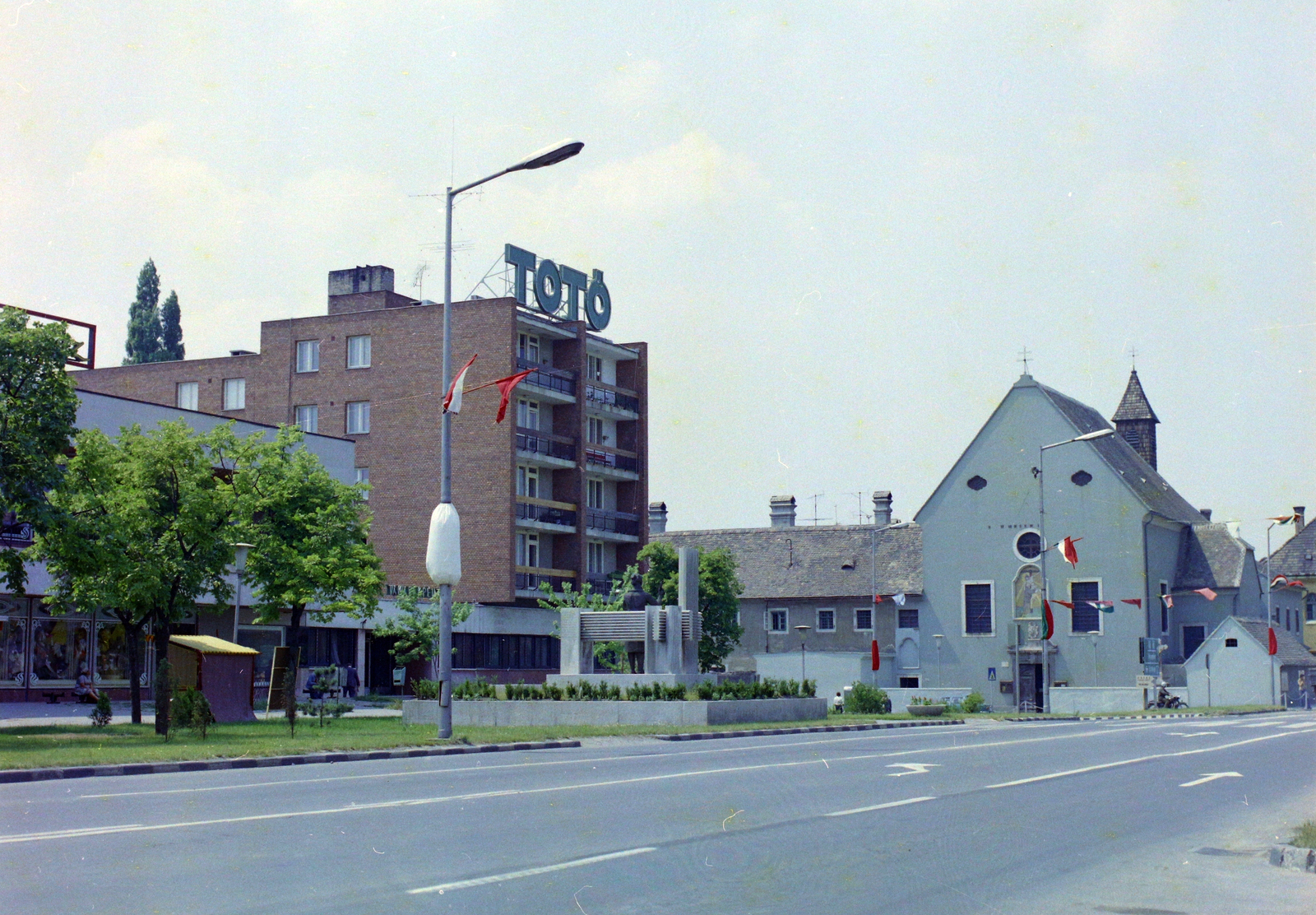 Magyarország, Tata, Ady Endre utca a Bartók Béla utca torkolatánál. A Szent Imre-templom előtt a Szövőnő című szobor (id. Kalló Viktor, 1977.)., 1978, UVATERV, színes, totó, Fortepan #99432