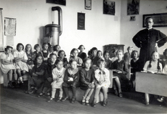 1930, Móra András, teacher, akimbo, arms crossed over the chest, sitting with hands on knees, classroom, cassock, iron stove, Fortepan #114958