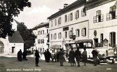 Ausztria, Mauterndorf, Marktplatz (Postplatz), balra a Szent Bertalan-templom, jobbra a Gasthof Post., 1932, Széman György, autóbusz, vendéglő, cégtábla, utcakép, életkép, várakozás, bőrönd, posta, utas, cégér, tetőcsomagtartó, Fortepan #115874