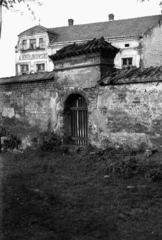 Poland, Niepołomice, ulica Piękna 2., a vértanúk templomának (Kościół Rzymskokatolicki pw. Dziesięciu Tysięcy Męczenników) kertje, háttérben Rynek 16 számú ház., 1947, Bogdan Celichowski, gateway, entrance, Fortepan #119931