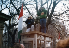 Magyarország, Budapest VIII., Múzeum körút a Magyar Nemzeti Múzeum bejáratától a Múzeum utca felé nézve. A fotósok múzeumkerti március 15-i ünnepség résztvevőit fényképezik a telefonfülke tetejéről., 1989, Marics Zoltán, színes, telefonfülke, tüntetés, Budapest, fotóriporter, leleményes, pulóver, címer, Fortepan #131443