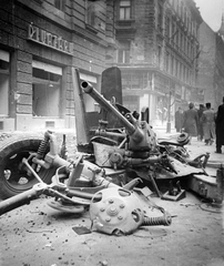 Magyarország, Budapest VII., Rákóczi út, háttérben a Hársfa utca sarkán álló ház látszik., 1956, Nagy József, forradalom, járókelő, utcakép, járműroncs, ágyú, üzletportál, épületkár, Budapest, légvédelem, légvédelmi ágyú, Fortepan #13457