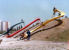 Magyarország, Budapest XI., játszótér a mai Bikás park területén. Háttérben a Tétényi út 25-27. számú panelház, jobbra a Tétényi úti (később Szent Imre) kórház., 1981, Hlatky Katalin-Főkert, színes, lakótelep, csúszda, Budapest, Fortepan #141288