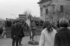 Magyarország, Monor, Kossuth Lajos utca, május 1-i ünnepség a megyei pártbizottság (később könyvtár) előtt, a szovjet hősi emlékműnél. Háttérben a katolikus templom, 1968, Péterffy István, templom, zászló, mikrofon, dobogó, jelmondat, pódium, Fortepan #141684