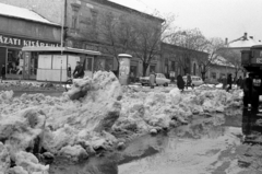 Hungary, Monor, Kossuth Lajos utca a Petőfi Sándor utca felé nézve, balra a 79. számú ház., 1969, Péterffy István, winter, puddle, ad pillar, number plate, clothing store, snow piles, paper shop, Fortepan #142460