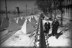 Magyarország, Budapest V., Dunakorzó, tankakadályok a villamossíneken, háttérben a lerombolt Széchenyi Lánchíd. Jobbra a kiégett Dunapalota / Ritz szálló., 1945, Vörös Hadsereg, harckocsi akadály, Budapest, fasor, úriember, hölgy, kabát, hídroncs, Fortepan #175142