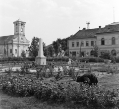 Magyarország, Csanádpalota, Kelemen László tér, az emlékoszlopot 1888-ban az Országos Színész Egyesület állította, Kelemen László az első magyar színigazgató, színműíró tiszteletére. Háttérben a Nepomuki Szent János-templom és a mai Polgármesteri Hivatal épülete., 1964, Bojár Sándor, Fortepan #177766