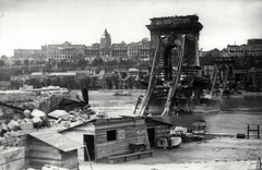 Magyarország, Budapest I.,Budapest V., a lerombolt Széchenyi Lánchíd pesti hídfője, háttérben a budai Vár., 1945, Fortepan, háborús kár, Budapest, hídroncs, rakpart, folyópart, palota, bódé, Fortepan #186689