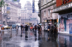 Magyarország, Budapest VII., Erzsébet (Lenin) körút, a Bástya mozi elöl a Nagykörút - Rákoczi út kereszteződése felé nézve., 1983, Fortepan/Album040, Budapest, utcakép, szemetes, moziműsor, neon felirat, színes, esernyő, járókelő, Ibusz, eső, Csemege vállalat, Fortepan #188439