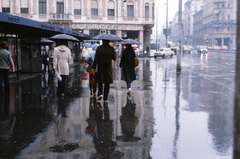 Magyarország, Budapest VII.,Budapest VIII., Rákóczi út, szemben az Akácfa utca torkolatánál az EMKE ház., 1983, Fortepan/Album040, Budapest, utcakép, háttal, tükröződés, színes, esernyő, járókelő, eső, Fortepan #188440