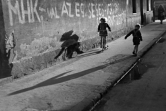 Hungary, Budapest VIII., Kis Stáció utca a Harminckettesek tere felé nézve, a kép jobb felső sarkában a Kisfaludy utca torkolata látszik., 1954, Kriss Géza, Budapest, kids, shadow, scooter, graffiti, pavement, MHK movement, puddle, Fortepan #191783