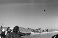 Magyarország, Budapest IX., Szabadság híd, háttérben balra a Fővám (Dimitrov) tér, Marx Károly Közgazdaságtudományi Egyetem (később Corvinus Egyetem), jobbra a Közraktár utca. A Bedobás kitalálója Dozvald János fotóművész, újságíró repteti fényképezőgépét. A felvétel az évente megtartott Bedobás / felesleges tárgyak Dunába dobása alkalmával készült., 1977, Gábor Viktor, Budapest, Fortepan #194205