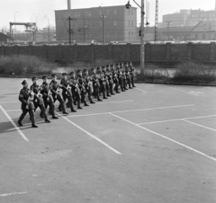 Magyarország, Budapest XIV., Dózsa György út, április 4- díszszemlére készülő katonák a Népstadion melletti parkolóban. Jobbra a Keleti pályaudvar külső vágányai és a Kerepesi úti "Százlábú híd" mögött az Országos (később Taurus) Gumiipari Vállalat épületei., 1975, Bojár Sándor, Budapest, Kalasnyikov, gépfegyver, Fortepan #195197