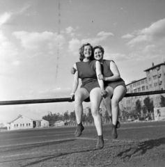 Magyarország, Budapest X., Maglódi út 4. sportpálya, a Kinizsi Sörgyár női röplabdacsapat tagjai, háttérben a Növényolaj és Szappangyár., 1955, Keveházi János, Budapest, karok a vállon, mosoly, nő, sportoló, korláton ülni, Fortepan #197198