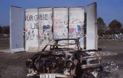 Németország, Berlin, 1990. október 3-án, az egyesülés napján a daruval felemelt és elégetett Trabant. A kiégett roncs és a berlini fal néhány meghagyott darabja a Brandenburgi kaputól nem messze, mementóként., 1990, Urbán Tamás, rendszerváltás, színes, modern művészet, Trabant-márka, járműroncs, Fortepan #213681