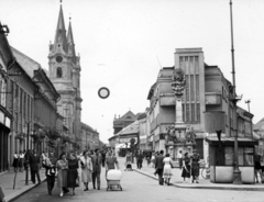 Szlovákia, Komárom, Szentháromság-szobor a Klapka György téren (námestie generála Klapku). Balra a Nádor utca (Palatinova ulica) és a Szent András-templom., 1954, Stuber Andrea, utcakép, járókelő, babakocsi, templom, pavilon, szentháromság szobor, Fortepan #229659