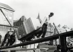 Szlovákia, Pozsony, rakodómunkások dolgoznak a Szlovák Nemzeti Múzeum (ekkor Szlovák Honismereti Múzeum) előtti teherhajó-kikötőnél, háttérben a Fémipari Szakiskola (később Gépészeti Szakközépiskola / Stredná priemyselná škola strojnícka) épülete., 1933, Bor Dezső, talicska, daru, rámpa, rakodás, láda, betolás, kikötő, Fortepan #231374