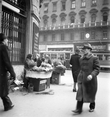 Magyarország, Budapest VIII.,Budapest VII., Erzsébet körút - Rákóczi út sarok a későbbi Éjjel-nappali közért előtt. Háttérben a Rákóczi út 39-es számú ház., 1943, Lőrincze Judit, reklám, kalap, cégtábla, könyvesbolt, villamos, virágárus, Bocskai-kabát, Julius Meinl-márka, Budapest, Fortepan #24584