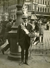 Magyarország, Budapest VIII., Blaha Lujza tér, háttérben a Népszínház utca - József körút sarok. Előtérben egy hadijelvény árus 1914. augusztusában, az I. világháború kitörése utáni hetekben., 1914, Országos Széchényi Könyvtár, Müllner János, Budapest, zászló, keménykalap, gyűjtemény, Fortepan #256069