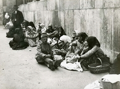 Magyarország, Budapest VIII., Vas utca 9-11., a felvétel a laktanyává átalakított Felső Kereskedelmi Fiúiskola előtt készült, 1914. augusztusában. Vidékről bevonuló népfelkelők és hozzátartozóik az I. világháború kitörése utáni mozgosítás idején., 1914, Országos Széchényi Könyvtár, Müllner János, Budapest, földön ülés, népviselet, várakozás, fejkendő, Fortepan #256232