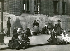 Magyarország, Budapest VIII., Vas utca 9-11., a felvétel a laktanyává átalakított Felső Kereskedelmi Fiúiskola előtt készült, 1914. augusztusában. Vidékről bevonuló népfelkelők és hozzátartozóik az I. világháború kitörése utáni mozgosítás idején., 1914, Országos Széchényi Könyvtár, Müllner János, Budapest, nők, földön ülés, Fortepan #256247