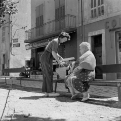 Franciaország, Cassis, Place de la République, balra a Rue Raphaël Ponson torkolata., 1958, UWM Libraries, Eugene Vernon Harris, Best of, képarány: négyzetes, francia felirat, vállkendő, nadrág, fonott táska, péksütemény, Fortepan #259174