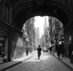 Franciaország, Rouen, Rue du Gros Horloge, az Óratorony (Le Gros-Horloge) átjárójából a Place de la Cathédrale felé. Háttérben a székesegyház (Cathédrale Notre-Dame-de-l'Assomption)., 1958, UWM Libraries, képarány: négyzetes, utcakép, boltív, átjáró, kerékpár, Fortepan #259183