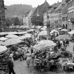 Németország, Freiburg im Breisgau, Münsterplatz, előtérben a Georgsbrunnen, balra a Freiburger Münster déli oldalfala, a kettő között a Historisches Kaufhaus kéttornyos épülete látható., 1958, UWM Libraries, piac, napernyő, csíkos ruha, virágárus, kút, NSZK, képarány: négyzetes, Fortepan #259305