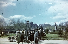 Hungary, Budapest V., Petőfi tér, Petőfi Sándor szobra (Huszár Andor, 1882.), háttérben a Királyi Palota (később Budavári Palota)., 1944, Kovács Györgyi, Budapest, lady, lawn, gentleman, hat, sculpture, motorcycle, bush, street lamp, Fortepan #263378