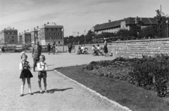 Magyarország, Budapest XI., park a Feneketlen-tó mellett. Szemben a Tas vezér utca. Jobbra a Villányi úton a Kertészeti és Szőlészeti Főiskola épülete (később Szent István Egyetem, majd Magyar Agrár- és Élettudományi Egyetem, Budai Campus)., 1958, Ábrahám Katalin és László, Budapest, kisfiú, kislány, ünneplő ruha, pad, park, Fortepan #266597