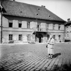 Hungary, Óbuda, Budapest III., Fő tér, a háttérben a 4. számú épület, jobbra a Kórház utca., 1955, Vozárik Edit, lady, house, Budapest, cornerhouse, cobblestones, balcony, gate, street lamp, arch, costume, bullet hole, Fortepan #270106