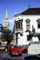 Magyarország, budai Vár, Budapest I., Úri utca, Hadik András lovasszobra (ifj. Vastagh György, 1937.), háttérben a Szentháromság utca sarkán a régi budai Városháza épülete, balra a Mátyás-templom., 1986, Saphier Herbert, Volkswagen Bogár, Volkswagen-márka, színes, rendszám, Hadik András-ábrázolás, lovas szobor, Budapest, Fortepan #287390