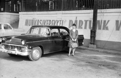 Magyarország, Diósgyőr, Miskolc, Vasgyár, 1. sz. hivatalház előtti parkoló. Ford Customline 1956-os modell., 1963, Fortepan, portré, amerikai gyártmány, Ford-márka, politikai dekoráció, hölgy, automobil, kézitáska, rendszám, Ford Fairlane, Ford Customline, Fortepan #29930