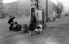 Magyarország, Budapest XI., Szent Gellért tér, balra a Gellért szálló állványzata., 1955, Fortepan, plakát, babakocsi, utcakép, életkép, hirdetőoszlop, hordó, oldalkocsis motorkerékpár, gyerekek, benzinkút, Budapest, Fortepan #30069