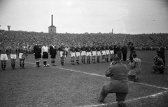 Magyarország, Budapest IV., Újpest, Megyeri út, UTE pálya, Magyarország - Olaszország (1:1) válogatott labdarúgó-mérkőzés. A magyar csapat: Balogh II Sándor, Puskás Ferenc, Lakat Károly, Kocsis Sándor, Budai II László, Szusza Ferenc, Bozsik József, Rudas Ferenc, Börzsei János, Deák Ferenc, Henni Géza, Szabó Antal segédedző, Lyka Antal edző. A játékosok fekete karszalagot viselnek, az FC Torino, az olasz bajnokcsapat május 4-i repülőgép szerencséttelenségben elhunyt játékosai és vezetői emlékére., 1949, Kovács Márton Ernő, filmforgatás, sajtófotó, sport, labdarúgás, fényképezőgép, filmkamera, Budapest, futballcsapat, sportbíró, Fortepan #33168