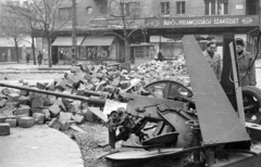 Magyarország, Budapest XI., Fehérvári út, szemben a Vásárhelyi Pál utca torkolata, jobbra a Móricz Zsigmond körtér, a Váli utca sarkáról nézve., 1956, Nagy Gyula, cégtábla, felirat, forradalom, barikád, fegyver, kockakő, gépágyú, Budapest, Fortepan #40035