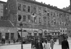 Magyarország, Budapest I., Széna tér 1/a., 1956, Nagy Gyula, háborús kár, cégtábla, forradalom, magyar gyártmány, járókelő, teherautó, bódé, Csepel-márka, gyógyszertár, lámpaoszlop, hentesüzlet, épületkár, Csepel D-352, Csepel B-350/D-350, Budapest, élelmiszerbolt, Közért Vállalat, Fortepan #40047