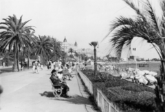 Franciaország, Cannes, a Croisette körút (Boulevard de la Croisette), Carlton Hotel felé nézve., 1934, MZSL/Ofner Károly, zászló, napernyő, járókelő, sétány, bódé, pálmafa, stég, pad, Fortepan #42181