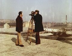 Magyarország, Budapest XIII., Madarász Viktor utca 5-7., Schiffer Pál filmrendező és Andor Tamás operatőr. Háttérben a Váci úti Akkumulátor és Szárazelemgyár., 1975, Schiffer Pál, színes, látkép, kémény, gyár, filmkamera, állvány, gyárkémény, Budapest, Fortepan #44640