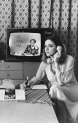 Magyarország, Rák Kati színésznő, háttérben a televízió képernyőjén Vitray Tamás., 1979, Rádió és Televízió Újság, Saphier Herbert, telefon, televízió, toll, TV műsor, képernyőfotó, Fortepan #56387