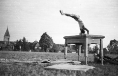 Magyarország, Pécs, Ifjúság útja 6., a Pedagógiai Főiskola (később Pécsi Tudományegyetem) sportpályája. Háttérben a Jézus Szíve (Pius) templom egyik tornya., 1958, Lipovits Károly, templom, katolikus, torna, tornaszőnyeg, tornaszer, kézenállás, mutatvány, Fortepan #61961